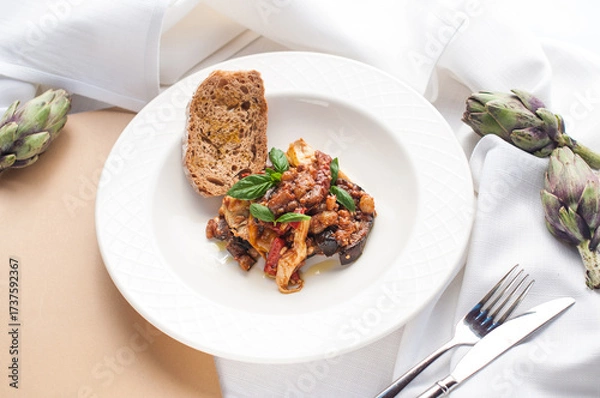 Fototapeta baked artichokes with eggplant in a white plate garnished with basil