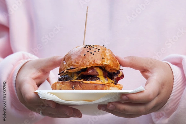 Fototapeta A close-up of young woman carrying a gourmet burger  with melted cheese on a tray with napkins at Karlin food festival in Prague.