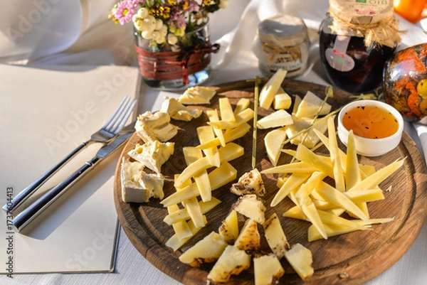 Fototapeta large cheese slices on a round wooden board