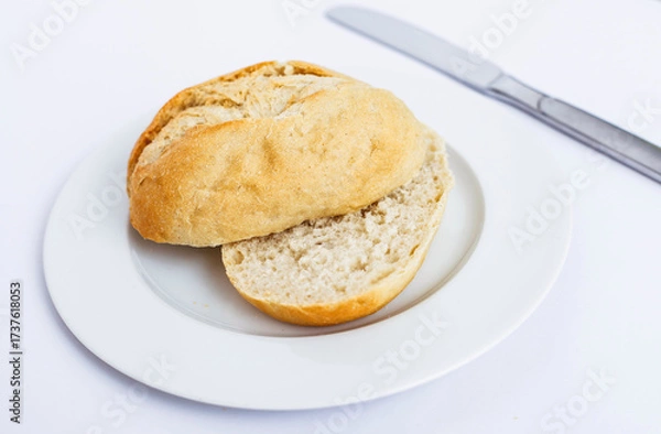 Fototapeta Sliced bread roll on a white plate with a knife.