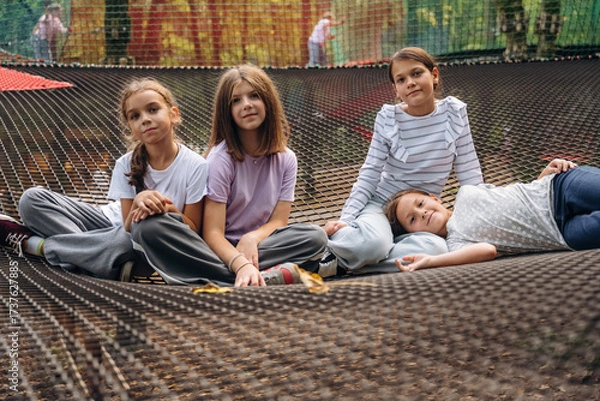 Obraz In casual clothes, relaxed, sitting. Kids are playing on the children's amusement ropes course