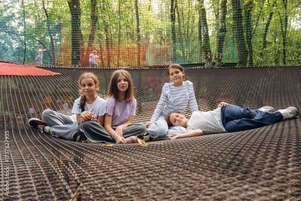 Obraz In casual clothes, relaxed, sitting. Kids are playing on the children's amusement ropes course
