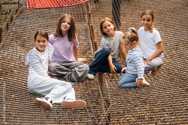 Obraz In casual clothes, relaxed, sitting. Kids are playing on the children's amusement ropes course