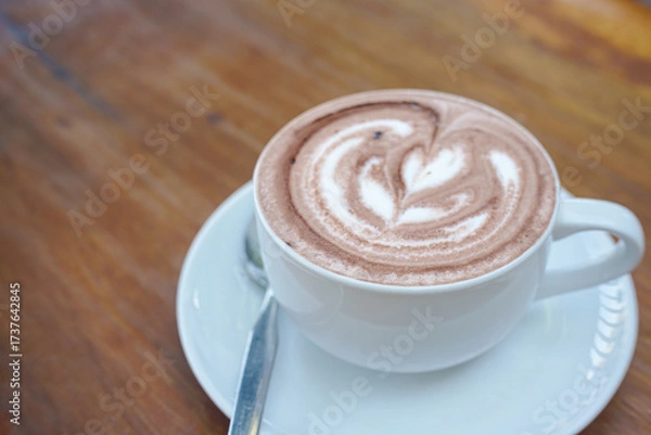 Fototapeta A cup of coffee with latte art on a wooden table