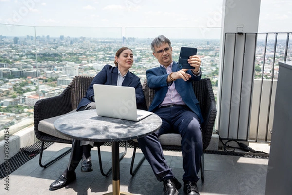 Fototapeta Two business people use tablet computer at rooftop office and city background	