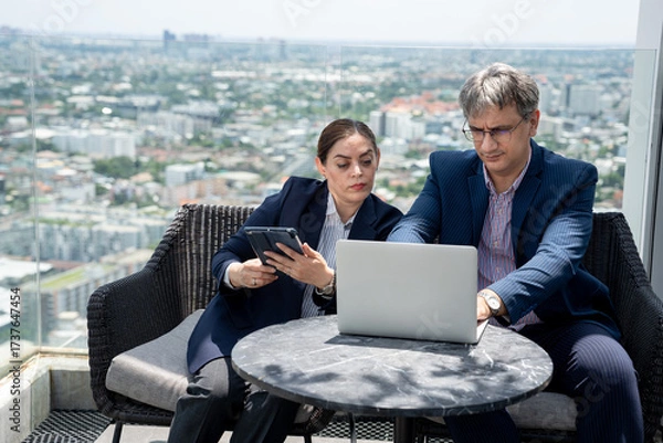 Fototapeta Two business people use tablet computer at rooftop office and city background	