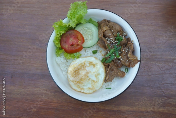 Fototapeta A vibrant bowl of rice topped with grilled beef, a fried egg, and colorful vegetables, served in a rustic dish