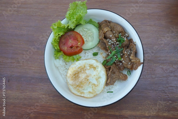 Obraz A vibrant bowl of rice topped with grilled beef, a fried egg, and colorful vegetables, served in a rustic dish