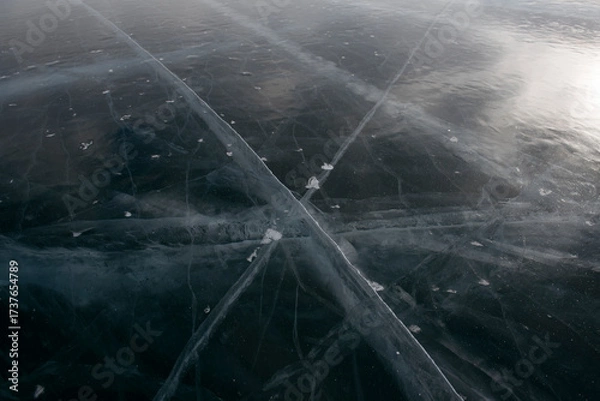 Fototapeta Intersecting cracks on dark frozen lake surface