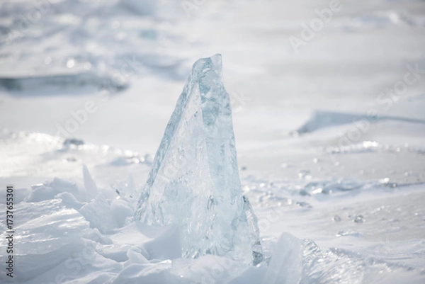 Fototapeta Close-up view of jagged ice fragments and snow layers shimmering in sunlight on a frozen winter surface with soft focus background.
