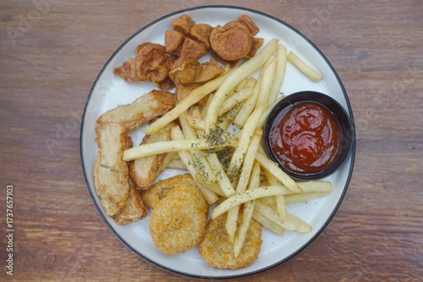 Fototapeta A delicious plate of golden fried snacks with ketchup and crispy fries on a wood background