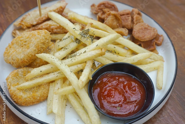 Fototapeta A delicious plate of golden fried snacks with ketchup and crispy fries on a wood background