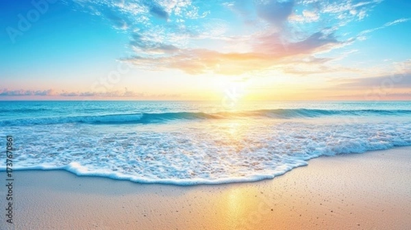 Fototapeta An idyllic beach sunset, where gentle waves meet the shore, illuminated by the warm glow of the setting sun. The composition features smooth sand with a subtle texture and a calm sea that reflects