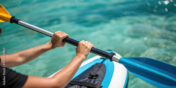 Fototapeta Hands holding inflatable kayak paddle on clear water with blurred background showing outdoor activity