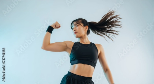 Fototapeta Athletic Asian woman flexing her bicep. Strong female athlete in sportswear showing her muscles. Fitness, power, and workout motivation concept