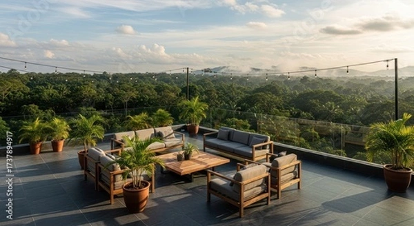 Fototapeta Relaxing rooftop lounge area boasts comfortable wooden furniture, potted plants, and string lights overlooking a lush green tropical forest scene under a partly cloudy sky at daytime.