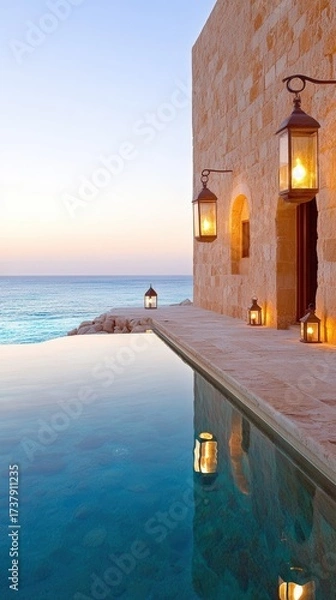 Fototapeta A tranquil seaside setting features a stone wall, glowing lanterns, and a serene pool reflecting the ocean at dusk, Ideal for promoting luxury travel, relaxation, or seaside retreats,