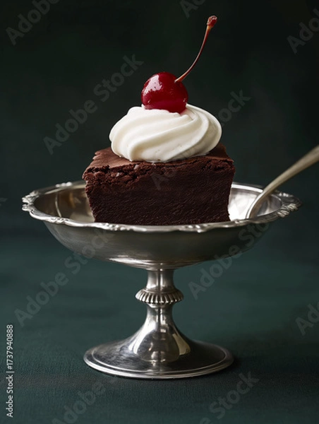Obraz A refined studio food photography shot featuring a decadent chocolate brownie elegantly placed in a silver dessert dish. The brownie is styled with a dollop of whipped cream and topped with a glossy r