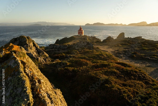 Fototapeta Punta Robaleira red lighthouse in Home cape at sunset in Rias Baixas zone in Galicia coast with Cíes islands in the background.