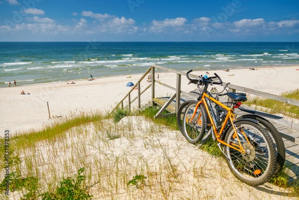 Fototapeta Two bicycles parked on a wooden ramp leading down to a wide, sunny beach of the Curonian spit, summer travel and active vacation
