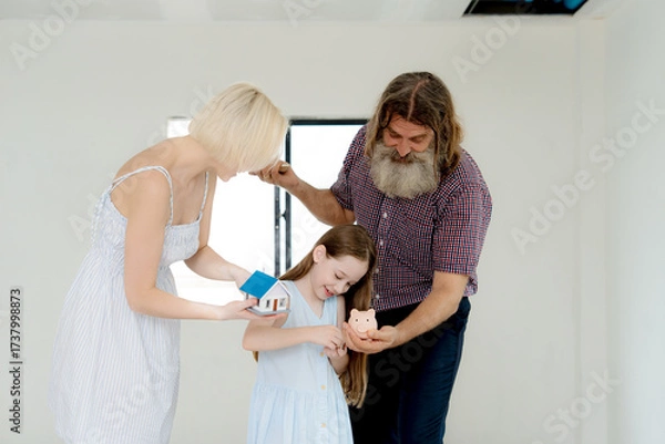 Fototapeta Happy father and mother guiding little daughter in saving money with piggy bank. Family concept of financial education, home ownership, investment, budgeting, and planning for secure future together.