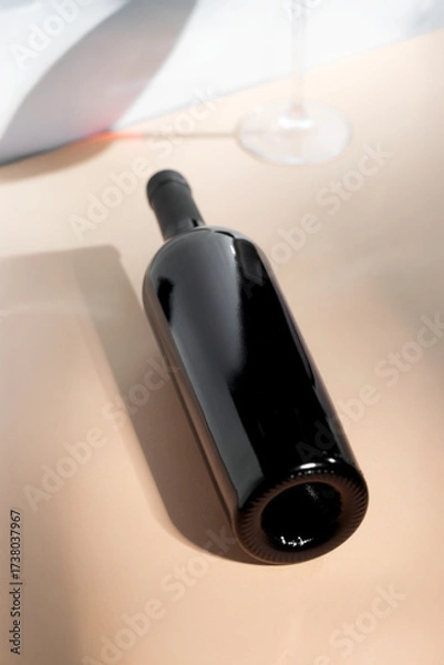 Fototapeta Red wine bottle mockup positioned on a smooth surface with elegant glassware in the background, ideal for branding and design projects showcasing beverage concepts