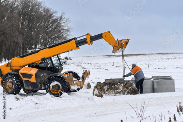 Fototapeta Installation of canalization rings with machine telehandler in winter conditions