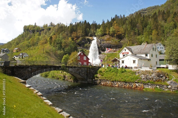 Fototapeta Steinsdalsfossen waterfall in the river of Steine - scenic landscape with cascade surounded by mountains and traditional norvegian, scandinavian houses