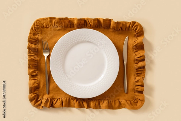 Fototapeta Autumn and Thanksgiving day table setting with empty white plate and orange towel on beige background. Top view. Mock up.