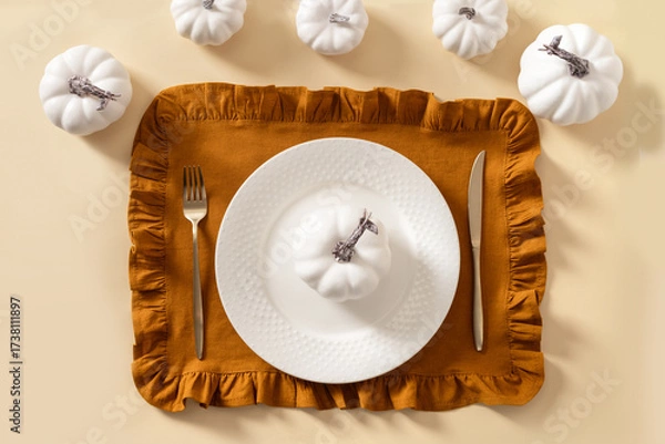 Fototapeta Autumn and Thanksgiving day table setting with plate decorated white pumpkins on beige table. Top view.
