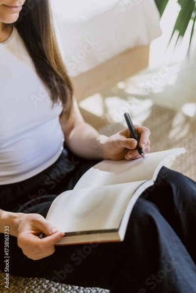 Fototapeta Woman practices morning pages writing in a bright and calm space for mental clarity