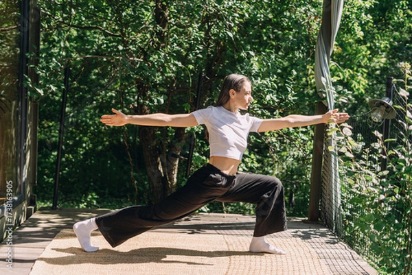 Fototapeta Woman practicing pilates in yoga pants surrounded by greenery in a garden