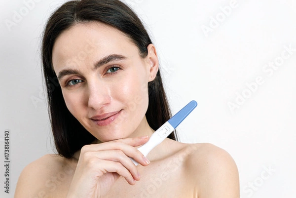 Fototapeta Young woman checks pregnancy test results with hopeful expression in home setting