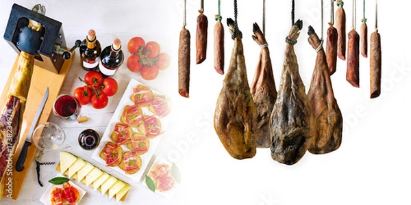 Fototapeta La mesa ibérica une tradición y sabor: jamón, vino y gesto culinario en escena compartida.Jamón en soporte, embutidos colgados, vino, pan con tomate, queso y tomates sobre mesa rústica.