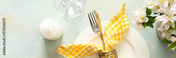 Fototapeta A charming table setting for spring includes a white plate with a yellow checkered napkin, fork, and knife neatly arranged among colorful flowers in bloom, banner