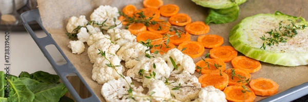 Fototapeta Cauliflower, carrots, and cabbage are sliced and arranged on a tray lined with parchment paper, ready for roasting with herbs in a warm kitchen setting, banner