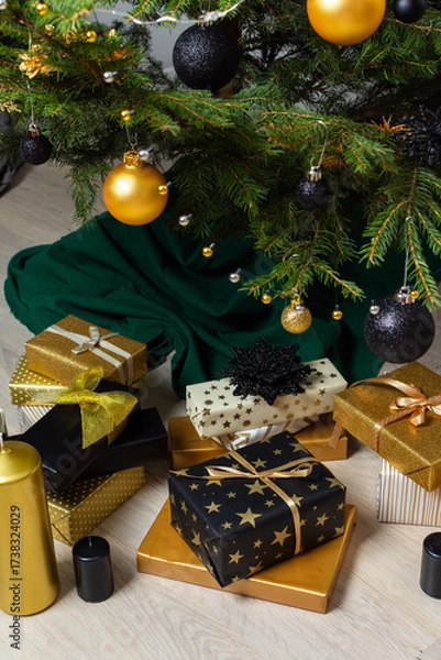 Fototapeta Luxurious gold and black gift boxes arranged beneath a Christmas tree, illuminated by glowing candles and adorned with elegant decorations, creating a chic holiday ambiance
