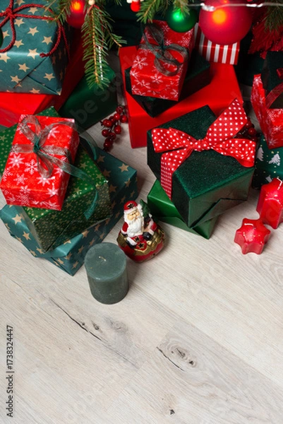 Fototapeta A festive display of green and red gift boxes under a beautifully decorated Christmas tree, complemented by candles and traditional ornaments, evoking warmth and holiday cheer