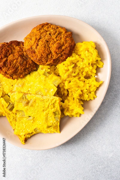 Fototapeta A vibrant plate features fluffy yellow rice, creamy rhubarb fried eggs, and crispy meat fritters, showcasing a hearty and flavorful meal perfect for any time of the day