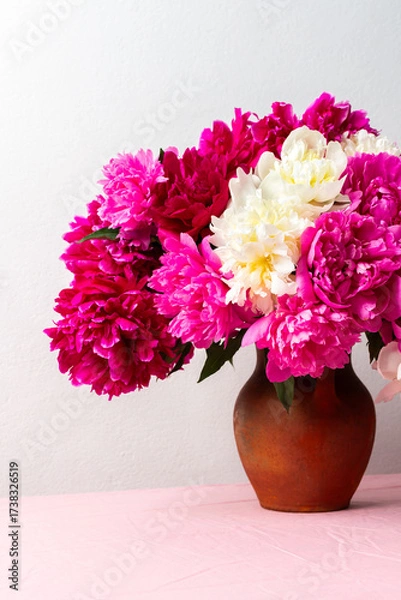 Fototapeta A vibrant arrangement of pink and white peonies fills a ceramic vase, placed on a soft pink tablecloth. The flowers add a cheerful touch to any room, ideal for spring decor