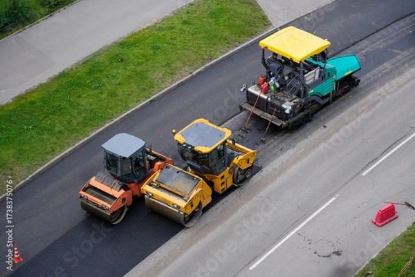Fototapeta Heavy machinery is at work paving a new road surface. Rollers and a paver are strategically positioned, ensuring a smooth finish. Workers are actively managing the equipment during the process