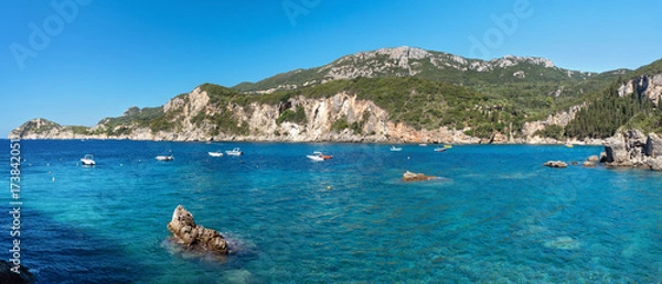 Obraz Bay of Liapades with many motorboats, sun shines on clear blue water, trees covered cliffs in background