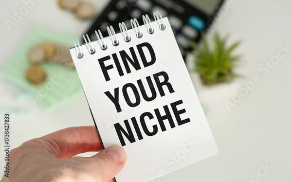 Fototapeta A person is holding a notebook with the word Find Your Niche written on it.
