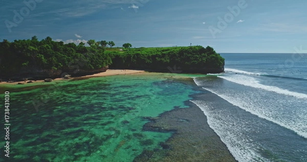Fototapeta Turquoise waves are gently crashing on the shore of Dreamland Beach in Bali, Indonesia, creating a breathtaking view of a tropical paradise with lush green vegetation and crystal-clear waters