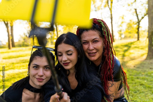 Fototapeta Women with varied styles capturing a group selfie together in a sunny park