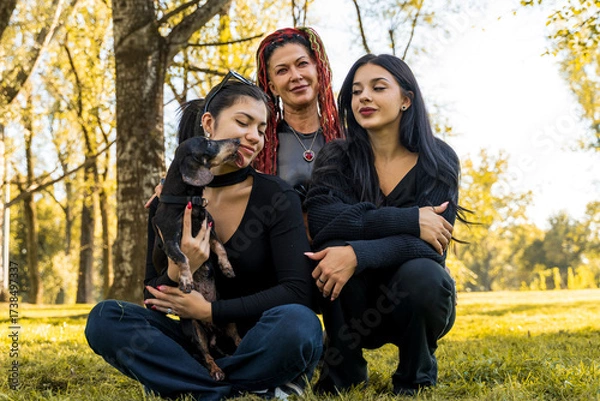 Fototapeta Mother and daughters enjoying leisure time with pet dachshund in a park