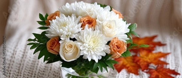 Fototapeta A bouquet with delicate blooms and warm-toned foliage sits in a glass jar on a wooden tabletop, illuminated by natural light