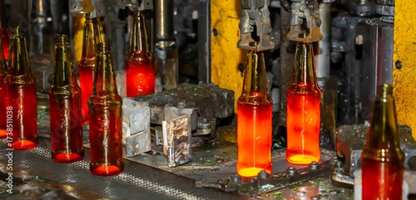 Fototapeta Glass factory, production of glass containers. Molten glass is blown into molds. Robotics in industry. Modern technologies, robotic machines produce products. Technological work at the plant.