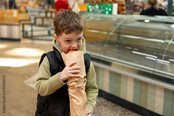 Fototapeta Little boy eating a freshly baked baguette bought from a bakery. High quality photo. Bread and breakfast concept,