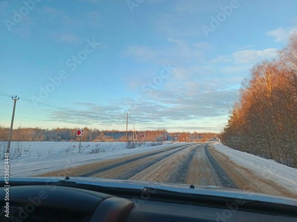 Fototapeta A car is driving down a snowy road.